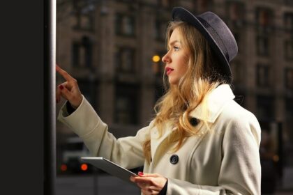 Young woman near digital screen in street at evening time